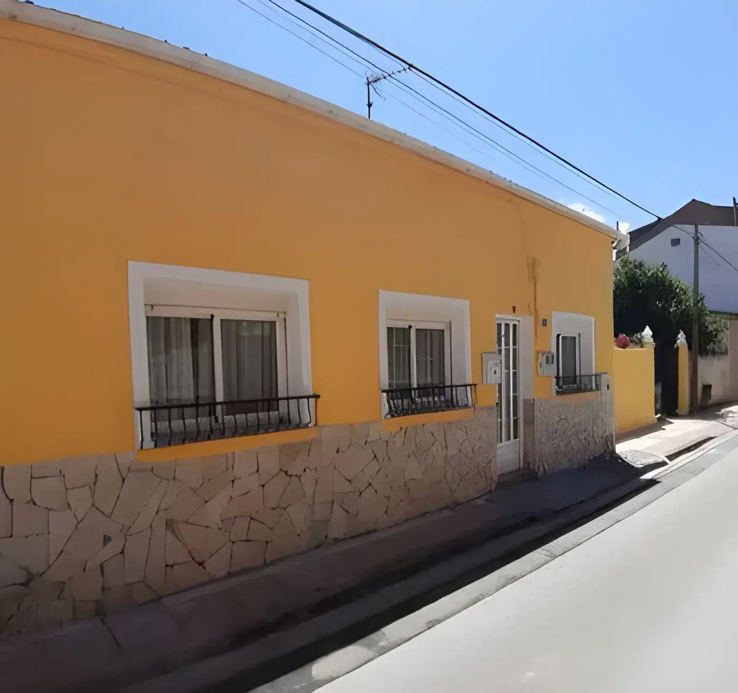 Los Pintores Alcorcón Fachada de casa tradicional pintada en color amarillo con zócalo de piedra